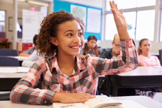 Young smiling girl raising her hand in class