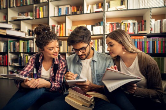 A group of high school students sitting on the floor in the library working on an assignment