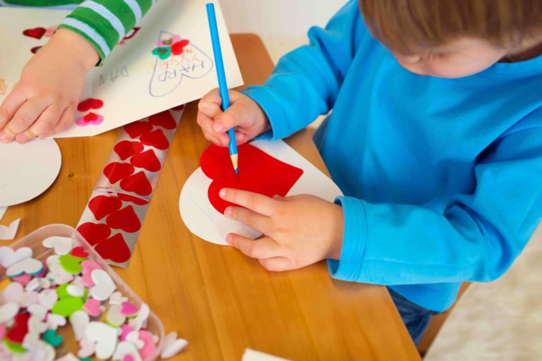 Young boy sitting at a table drawing on a red heart