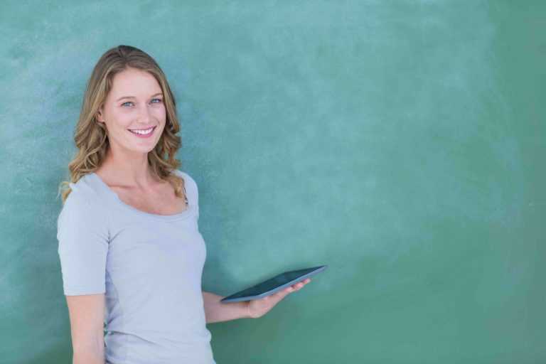 Female teacher standing by chalkboard holding a tablet