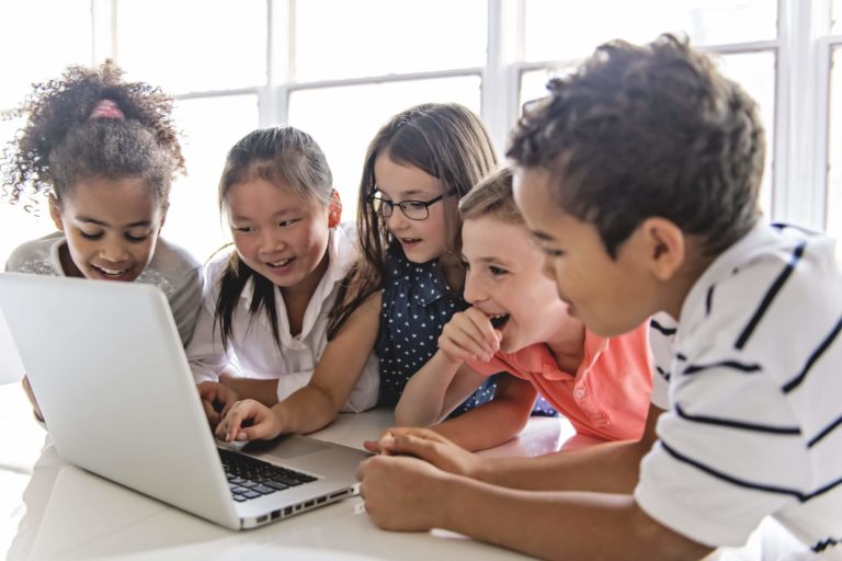 Group of young students huddled together around a laptop.