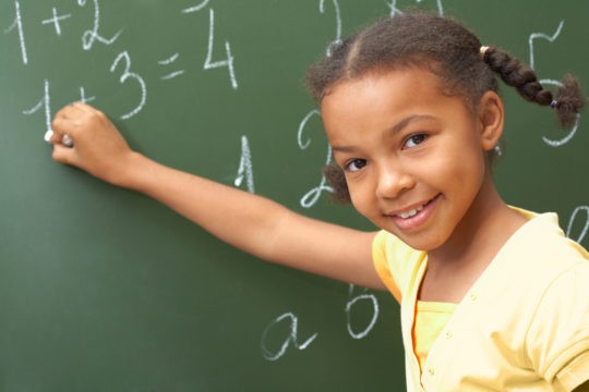 Young girl working on math problems at a chalkboard