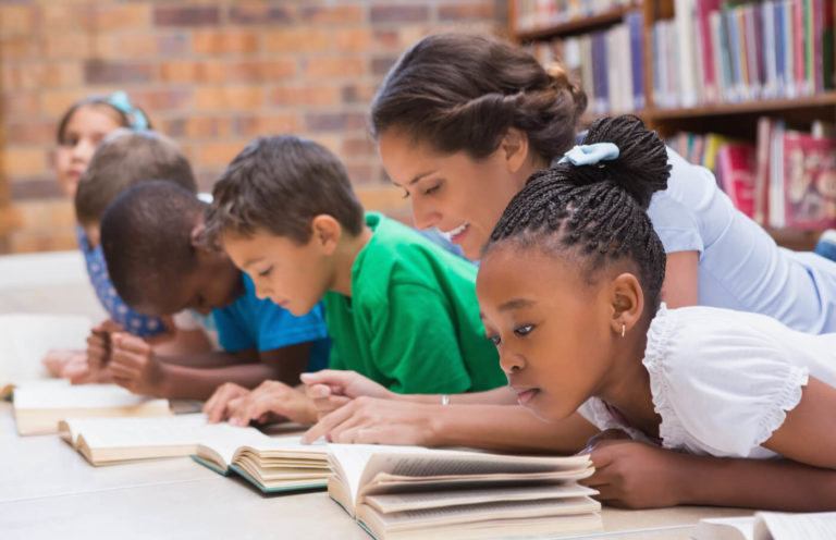 Several young students reading books on the floor together.