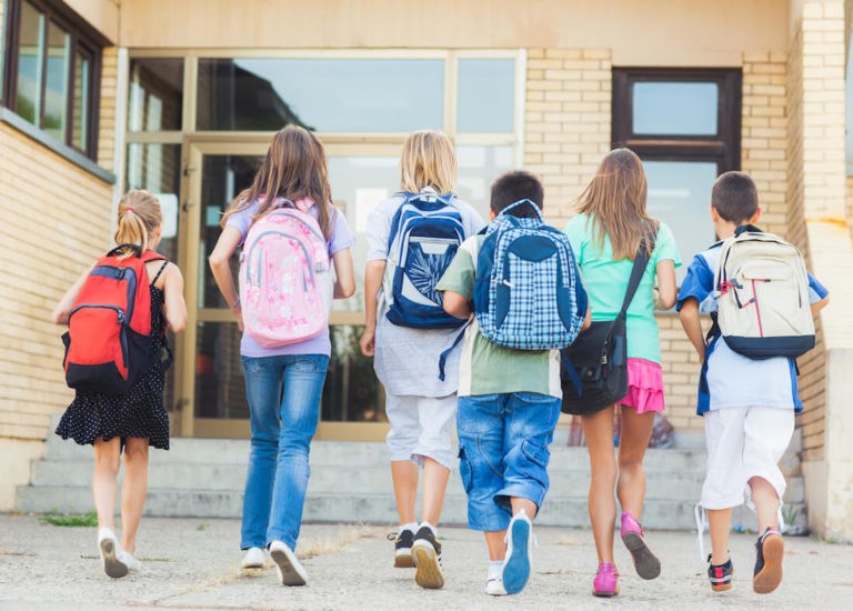 Group of students wearing backpacks approaching the school doors.