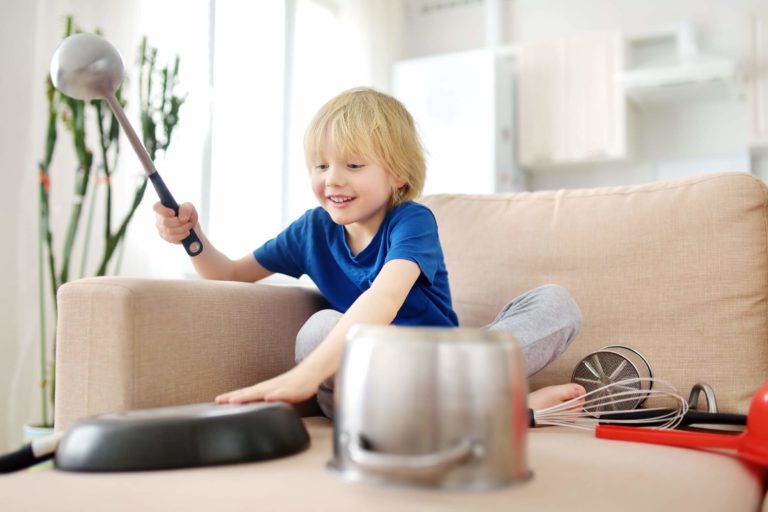 Young boy sitting on a couch playing with pots and pans to make music.