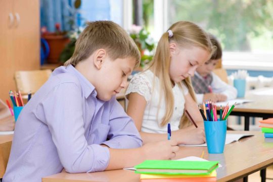 Two young students sitting at their desk writing on paper