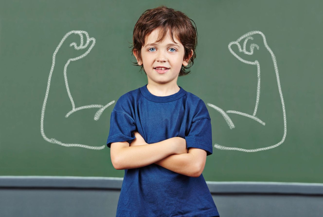 Young boy standing in front of chalk board with arms drawn on both sides of him