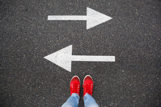 Pair of bright red sneakers standing before two arrow pointing opposite directions.