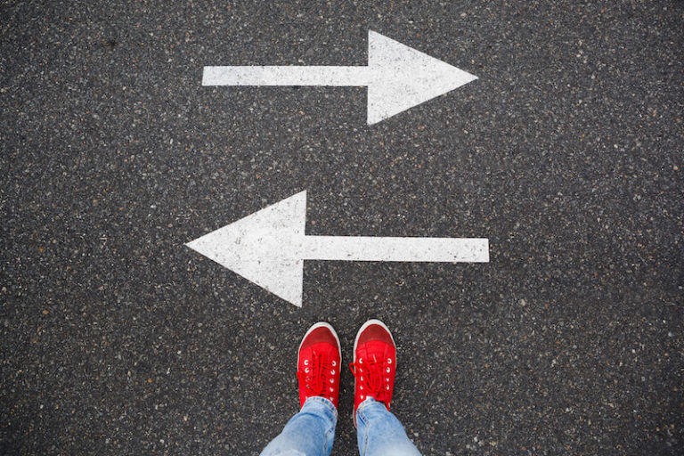 Pair of bright red sneakers standing before two arrow pointing opposite directions.