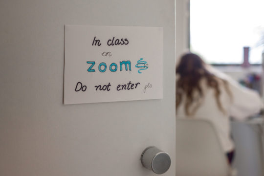 A students working at a desk with a sign on the door saying “in class on Zoom. Do not enter”