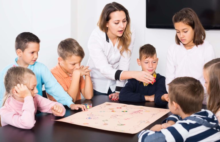 Group of young students playing a game together at a table with a teacher giving instruction.