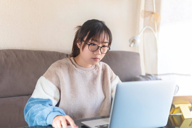 Teenaged girl sitting on a couch using a laptop.