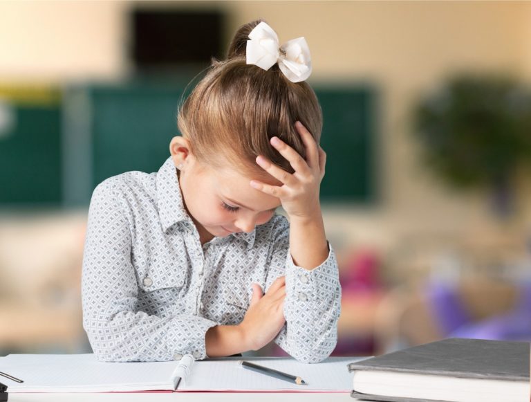 Young girl holding her head while sitting at a desk with a notebook and pencil.