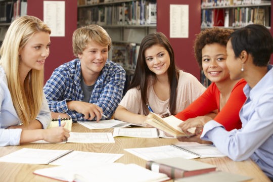 A group of high school students sitting at a table with books and paper working on a project