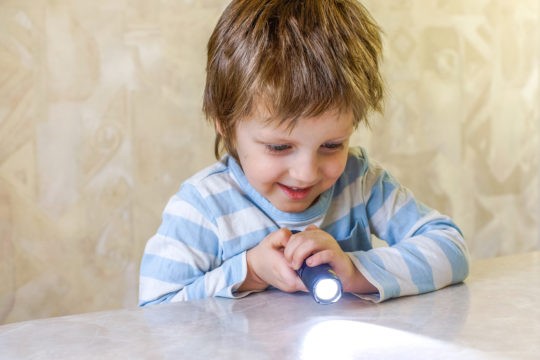 Young boy shining flashlight on a table