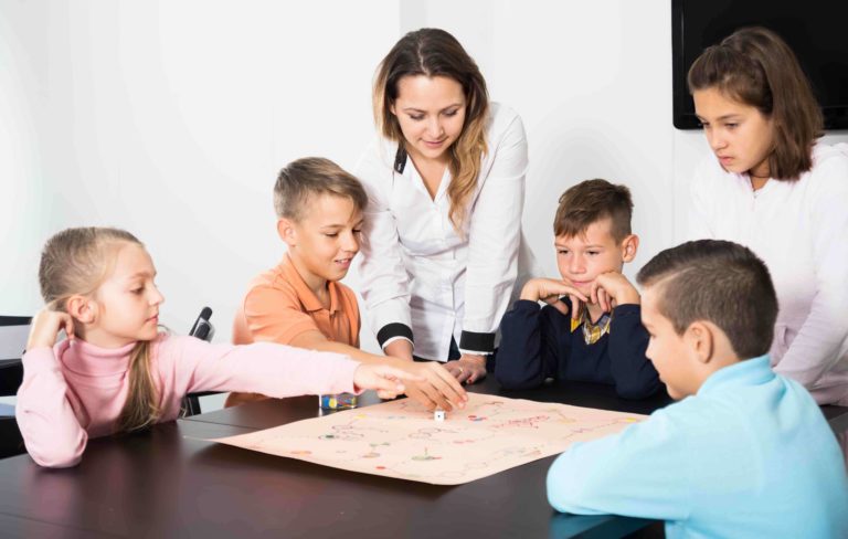 Teacher standing over a group of young students at a table playing a review game