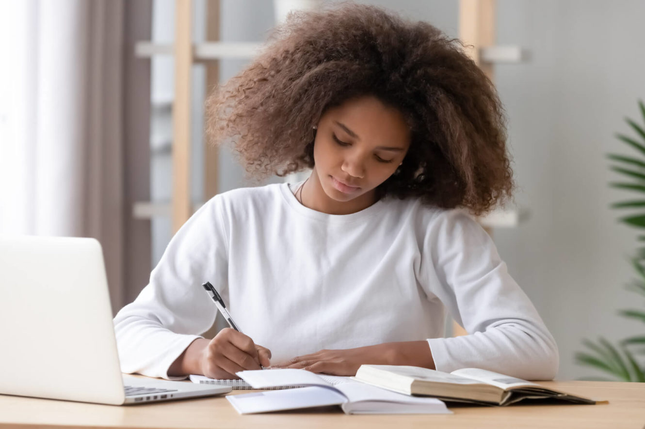 Female high school student with open laptop and writing in notebook