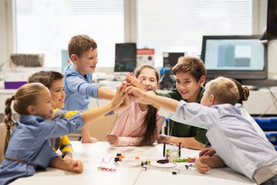 Small group of young students sitting at a table working on a project high-fiving each other.