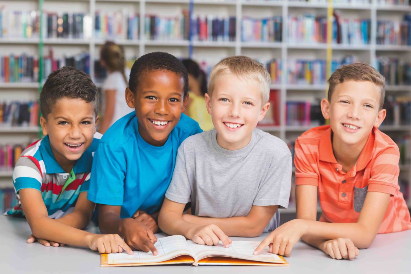 Three young boys smiling and pointing at an open book