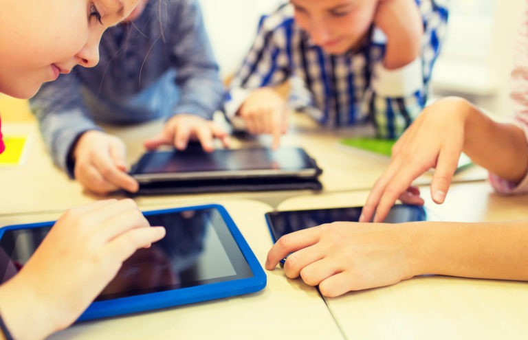 Group of students sitting at desks and using tablets.