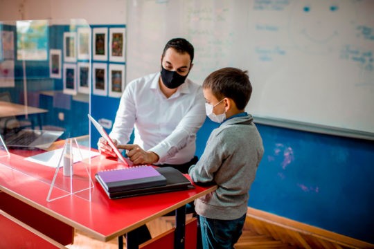 Teacher pointing something out on a paper to a young student.