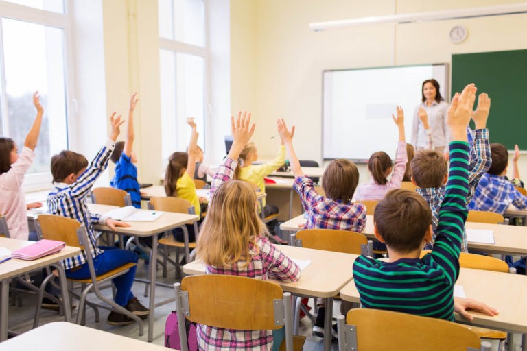 Group of students with hands raised in a classroom.