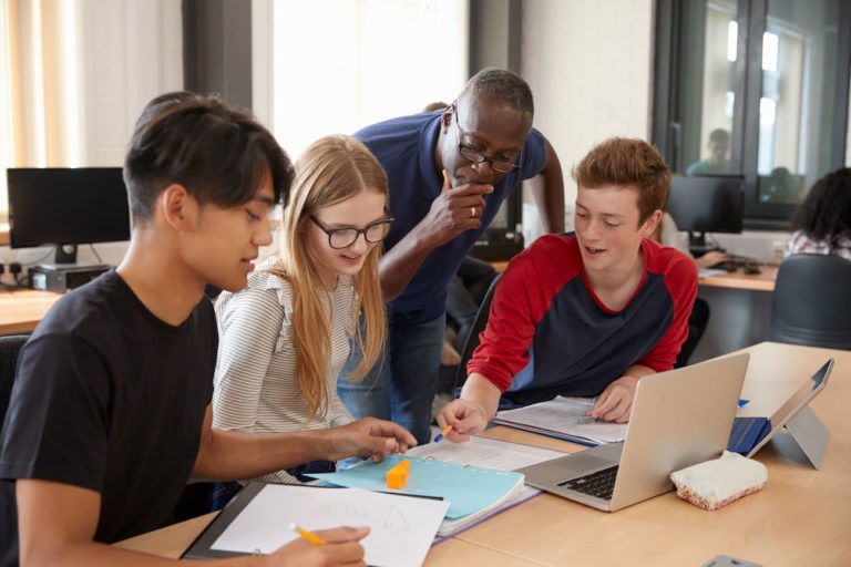 High school students working at a table together with a teacher checking in.