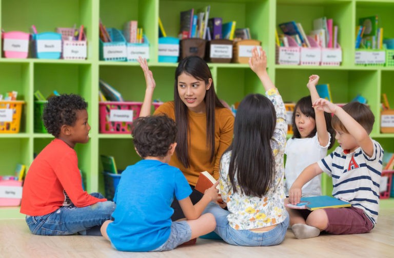 Teacher reading to a group of young students sitting on the floor in a classroom.