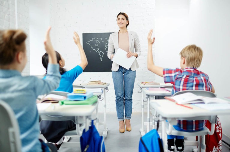 Young teacher standing at the front of a classroom full of young students.