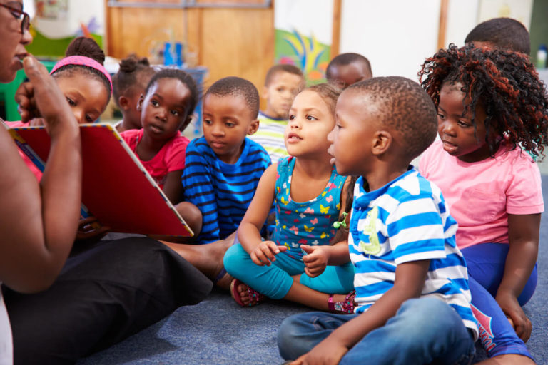 A teacher reading a book to a group of young students sitting on the floor.