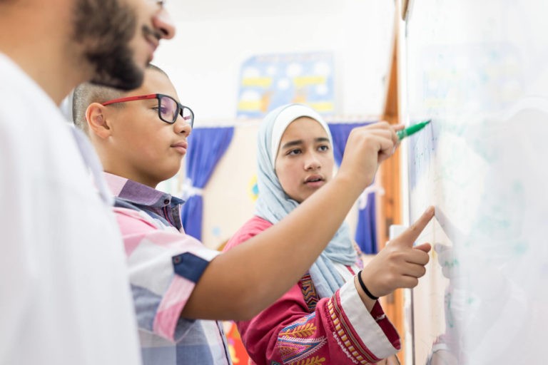 Two students standing at a white board demonstrating understanding.