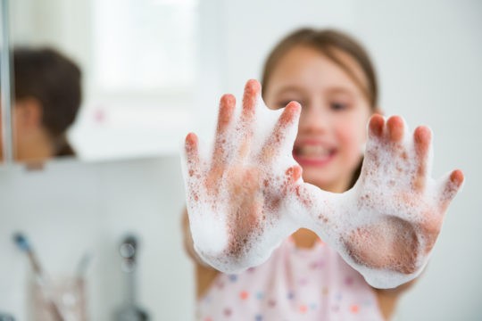 Young girl holding up her soapy hands while washing them and smiling.