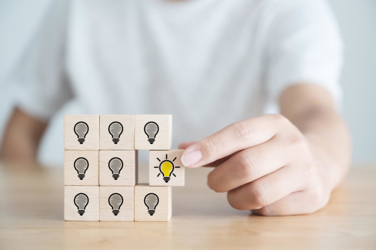 A boy picks a wooden cube with a lit up lightbulb icon on it, conceptualizing innovation and creativity.