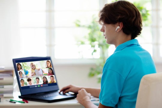 Teenage boy sitting at a desk participating in a virtual learning classroom.