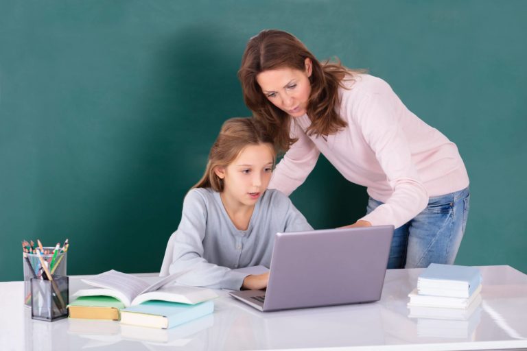 Teacher helping a young student working at a table with a laptop.