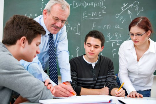 Teacher giving feedback to a group of students sitting at a table.