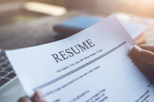 Someone holding a resume in front of an open laptop.