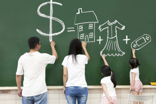 Family drawing money, house, clothes, and video games on a chalkboard