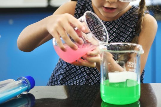 Young girl mixing colorful solutions in a science experiment.