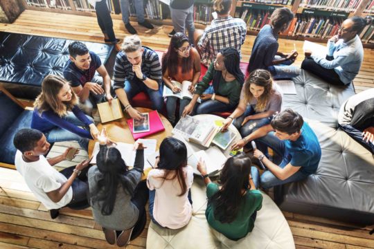 Group of students sitting together in the library working and talking.