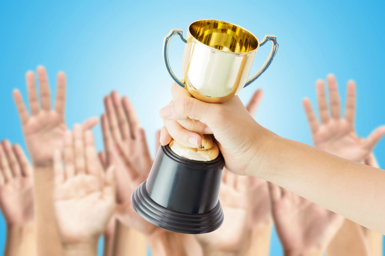 A group of hands raised with one hand in the middle holding a trophy