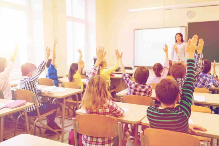 Young students sitting at desks raising their hands in a classroom