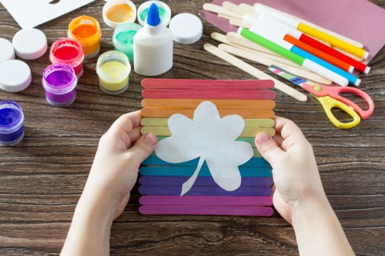 Child holding their rainbow art project with a clover on the front.