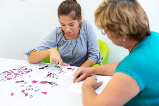 Teacher sitting at a table with a student working on worksheets.