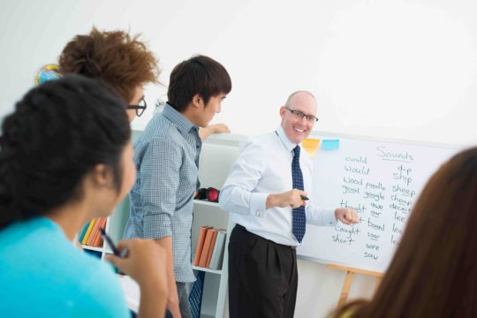 Male teacher playing a word game with students on a white board